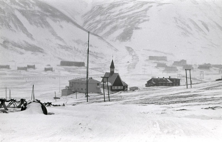 The settlement in Longyearbyen has moved around according to where the mines were found. This photo from about 1979-80 shows Svalbard church and the old hospital in the foreground. In the back you see Lia ("The hillside" - Left) and Haugen ("the hill" - right) with the Funktionærmessen (canteen for the white collared employees). Most of this will be visible on a walk in today's Longbyearbyen, but there are many more houses. The photographer is unknown. © Svalbard museum